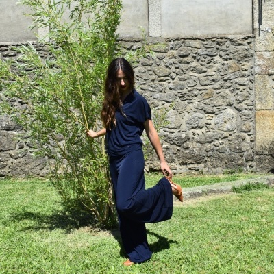 Mulher com roupa azul escura em relvado com parede de pedra ao fundo