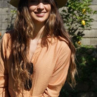 Mulher com camisa laranja, calças de ganga, chapéu de palha em ambiente exterior