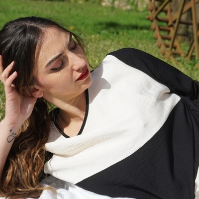 Mulher deitada na relva com camisola preta e branca e calças brancas