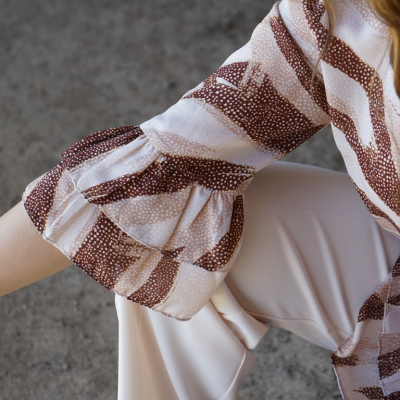 Manga de blusa com padrão riscas castanhas e rosa e calças largas creme em chão cinzento