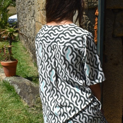 Pessoa de costas a usar pijama com padrão de ondas preto e branco ao ar livre junto a parede de pedra e plantas