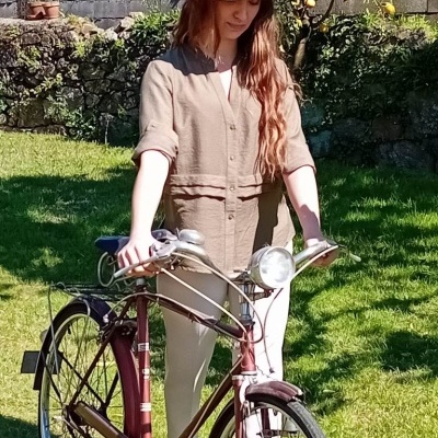Mulher com fato de linho bege e chapéu de palha segurando bicicleta vintage vinho no jardim