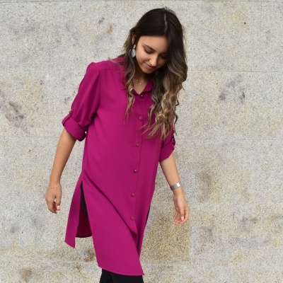 Mulher com vestido rosa fúcsia em frente a parede de pedra cinzenta