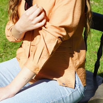 Pessoa com camisa laranja e calças de ganga sentada num banco de madeira na relva