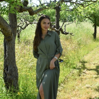 Mulher com vestido verde longo junto a árvore em campo verde