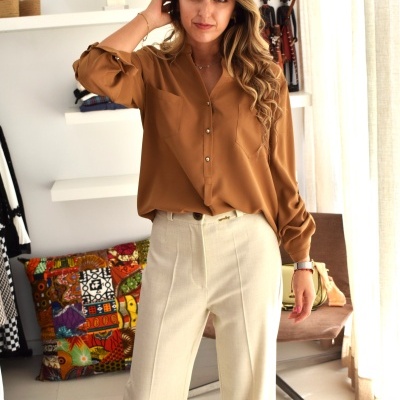 Mulher com camisa castanha e calças bege em interior com almofada colorida e estantes brancas