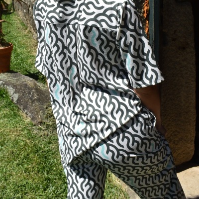 Conjunto de roupa com padrão geométrico preto e branco com detalhes azuis, usado por pessoa de costas no exterior.