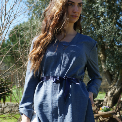 Blusa azul feminina com fita preta na cintura, usada ao ar livre com árvores ao fundo.