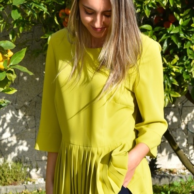 Blusa amarela feminina com saia plissada e mangas 3/4 em ambiente externo.