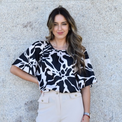 Blusa preta e branca com padrão abstrato com calças bege junto a parede de pedra