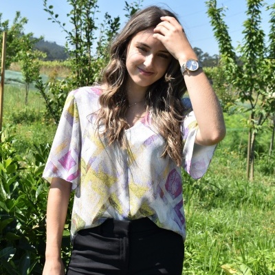 Mulher com blusa estampada colorida e calças pretas em ambiente natural