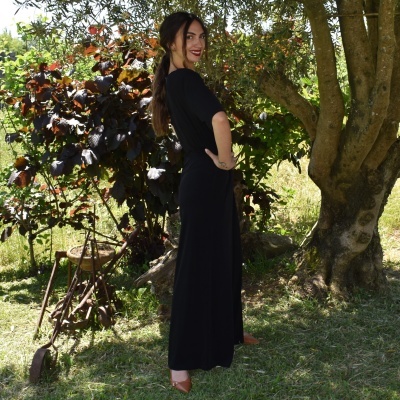 Mulher com vestido longo preto em jardim junto a árvore e ferramentas antigas