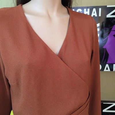 Blusa ou vestido castanho com decote em V em manequim, fundo com cartazes coloridos.