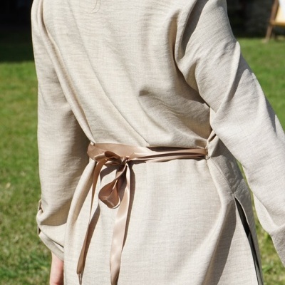 Casaco bege claro com cinto castanho amarrado, visto de costas ao ar livre