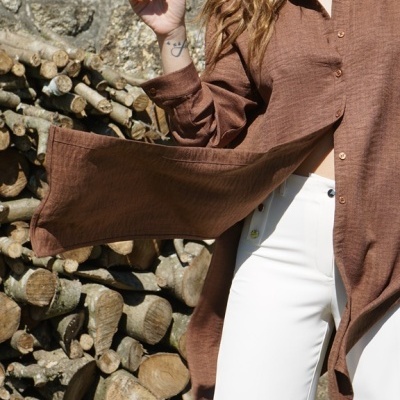Camisa castanha com textura e calças brancas em cenário exterior com pedra e lenha