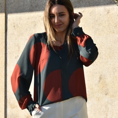 Blusa feminina com padrão de círculos em verde-escuro e castanho-avermelhado, usada com calças brancas