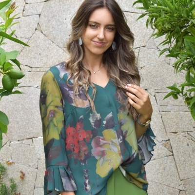 Camisola feminina transparente com estampa floral e mangas franzidas, parede de pedra e plantas ao fundo