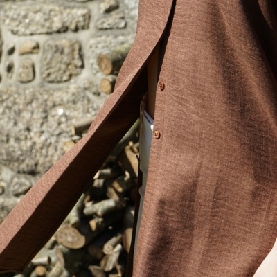 Casaco comprido castanho com botões ao ar livre perto de parede de pedra e lenha