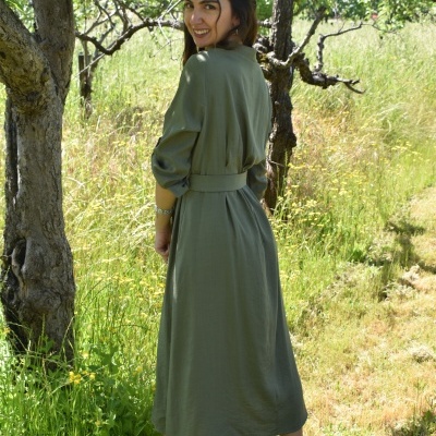 Mulher usa vestido verde-oliva comprido com cinto e ténis brancos numa paisagem natural ao ar livre