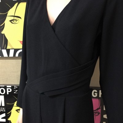 Macacão preto com decote em V e cinta larga na cintura em fundo com painéis coloridos de rostos estilizados