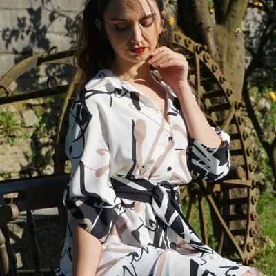 Vestido branco com padrão abstrato em preto e bege, modelo sentada no banco exterior.