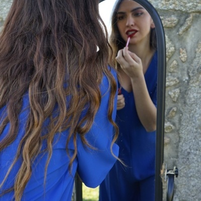 Mulher a aplicar batom vermelho em frente a espelho de corpo inteiro com estrutura preta