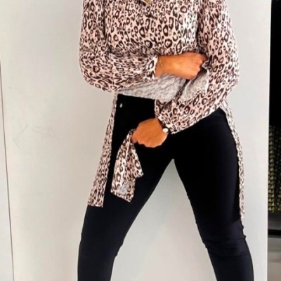 Mulher com camisa animal print, calças pretas e sapatos nude num fundo branco