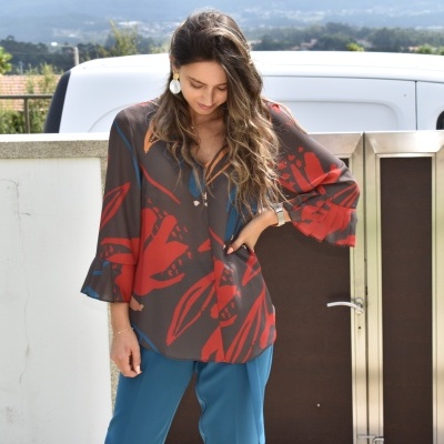 Blusa feminina castanho escuro e vermelho com padrão abstrato e mangas 3/4 vista ao ar livre