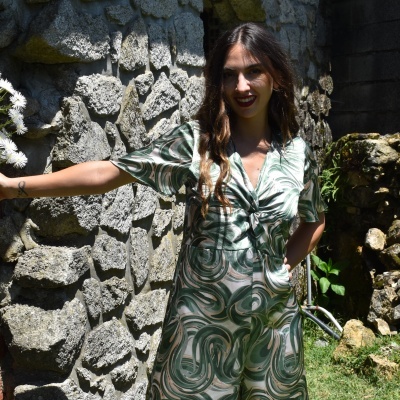 Vestido midi feminino verde com padrão abstrato usado por mulher junto a parede de pedra