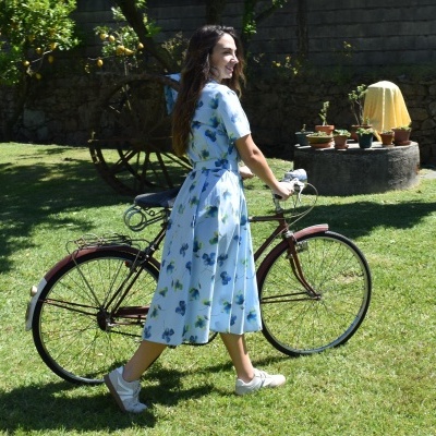 Mulher com vestido azul e bicicleta antiga em jardim verde