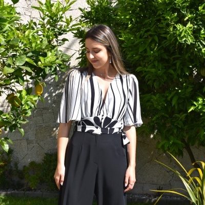Blusa branca com riscas pretas e calças pretas num jardim
