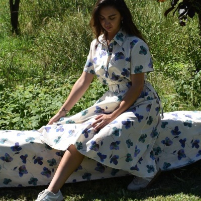 Mulher sentada num jardim a usar vestido floral branco com flores azuis e ténis brancos