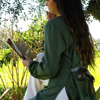Mulher sentada lendo livro vestindo blusa verde escura com fita preta e calças brancas ao ar livre