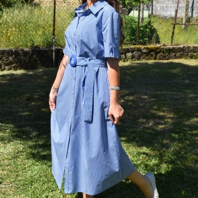 Mulher com vestido midi azul às riscas brancas num jardim, calçando sapatos de lona riscada.