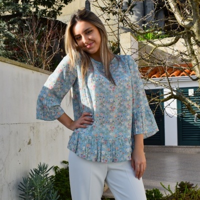 Blusa azul clara com flores e calças brancas usada por mulher em ambiente exterior