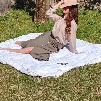 Mulher com roupa bege e verde sentada em cobertor branco na relva