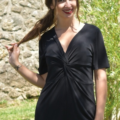 Mulher com vestido preto de tecido liso com nó no peito em cenário ao ar livre
