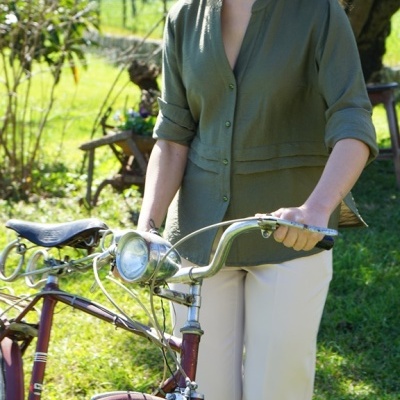 Mulher com camisa verde, calças brancas e chapéu de palha com bicicleta vermelha ao ar livre