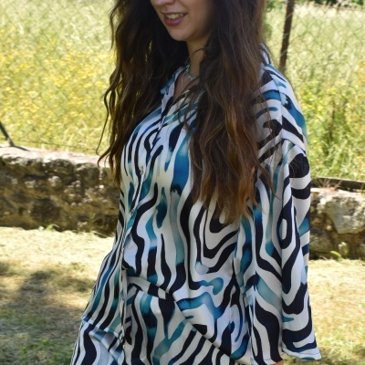 Mulher com macacão estampado abstraído azul, preto e branco em jardim com cerca metálica