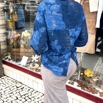 Pessoa de costas com blusa azul floral e calças cinza à frente de loja com base de mosaico