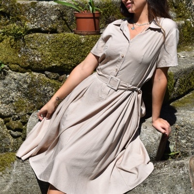 Vestido bege claro com cinto, gola de camisa e mangas curtas em ambiente exterior com degraus de pedra e plantas.