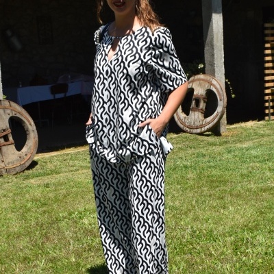 Mulher com conjunto de roupa preto e branco com padrão ondulado, óculos escuros, em gramado exterior