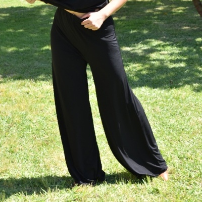 Pessoa com calças largas pretas e camisa preta num jardim com relva verde