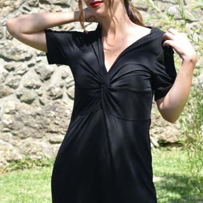 Mulher com macacão preto de tecido liso e detalhe torcido no peito em exterior