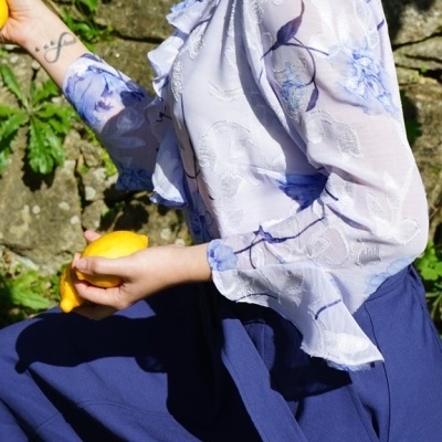 Blusa transparente com padrão floral azul e saia azul escura, modelo segurando limões ao ar livre