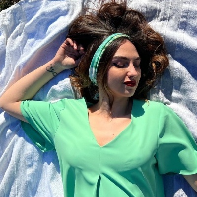 Mulher deitada com blusa verde e faixa de cabelo verde e branco