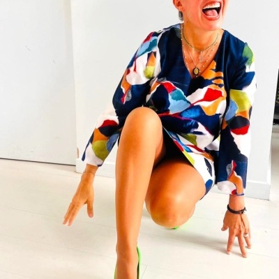 Mulher com vestido colorido, sapatos verdes de salto e óculos de sol em ambiente branco