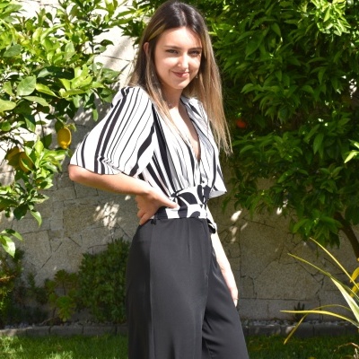 Mulher a usar blusa riscada preta e branca com calças pretas ao ar livre.