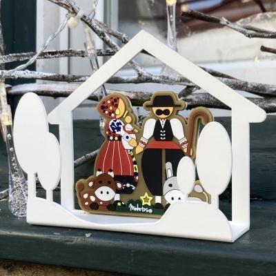 Enfeite decorativo com casal vestido tradicionalmente, burro e vaca dentro de estrutura branca em forma de casa