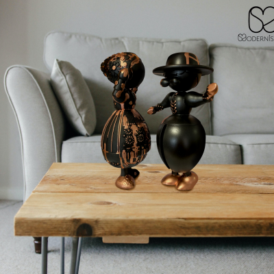 Dois bonecos decorativos pretos e dourados numa mesa de madeira com sofá cinzento ao fundo